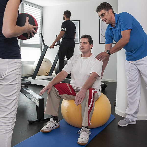 Mann auf Gymnastikball in der Physiotherapie